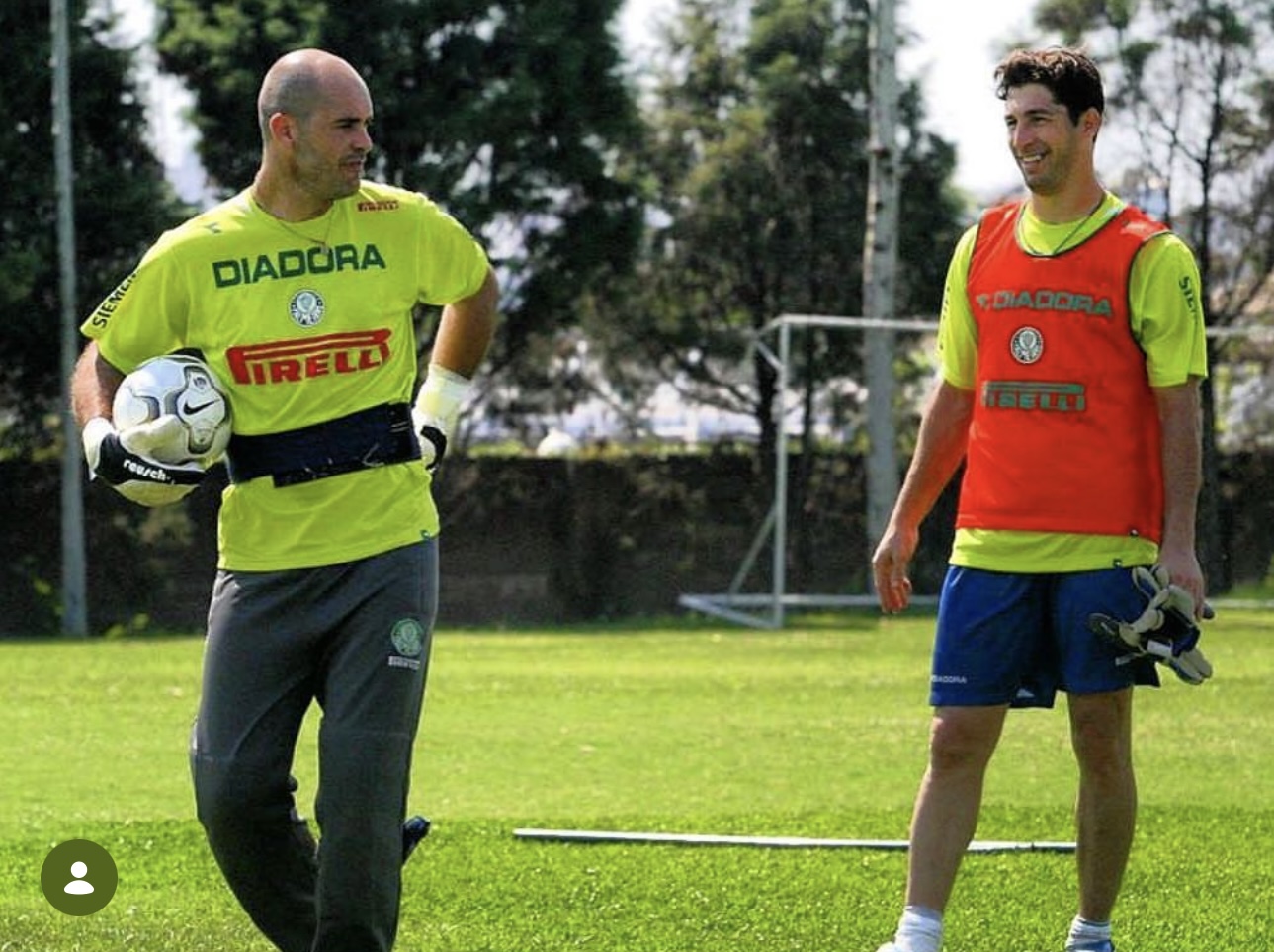 Marcos, de camisa amarela de treino e bola debaixo do braço, e Sérgio, de colete laranja e luvas na mão, sorrindo no gramado
