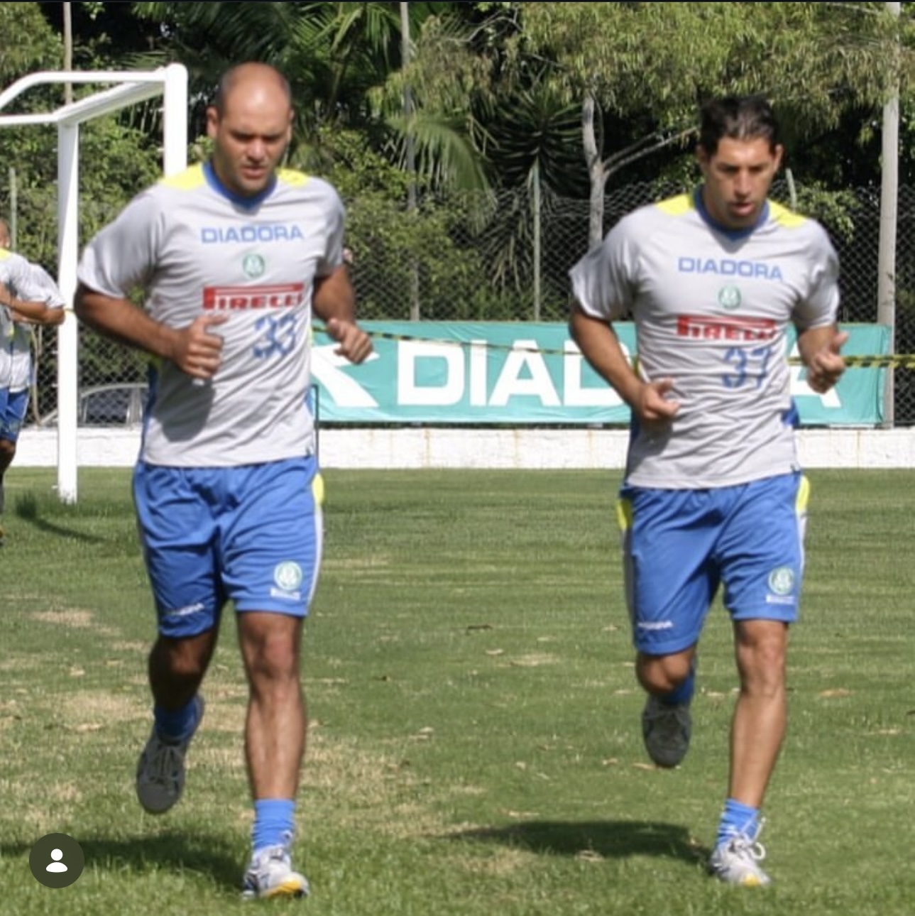 Marcos e Sérgio correndo lado a lado no gramado durante treino, de camisa branca e calção azul